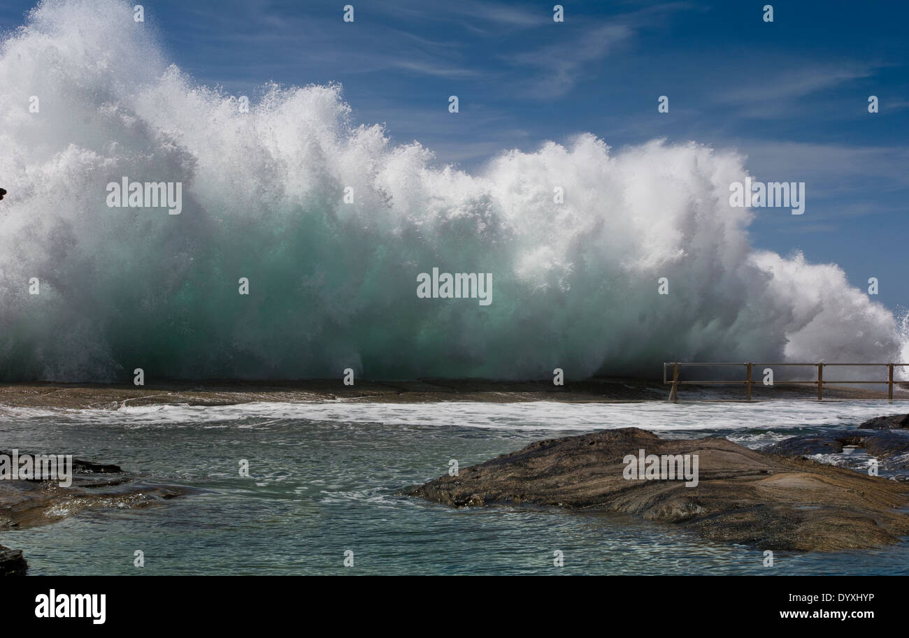 Grande onda schiantarsi contro le rocce sul lato di un oceano tidal piscina Foto Stock