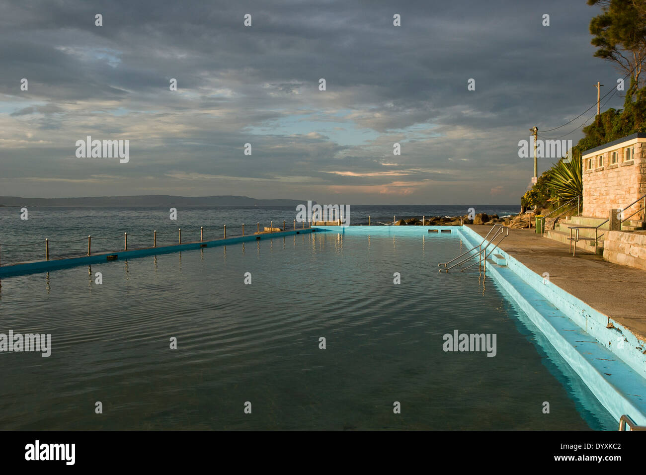 Ocean pool di marea integrato nel mare naturale-rocce. foto sul giorno ancora con soffici nuvole temporalesche & golden la luce solare sulla piscina e la costruzione Foto Stock