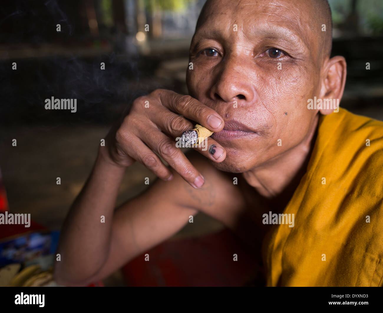 Cambogiano monaco buddista di fumare un sigaro handrolled realizzato con foglia sankai, accanto al tempio Bayon, Angkor Thom, Siem Reap, Cambogia Foto Stock