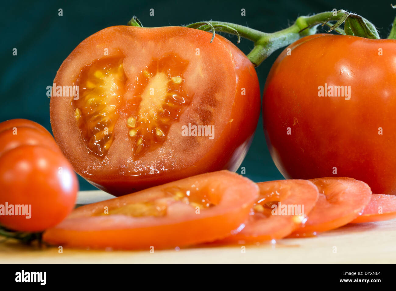 In prossimità dei quattro fette di pomodoro rosso su un tagliere di legno. Quattro pomodori interi e una metà pomodoro mostra di sementi e di carne Foto Stock