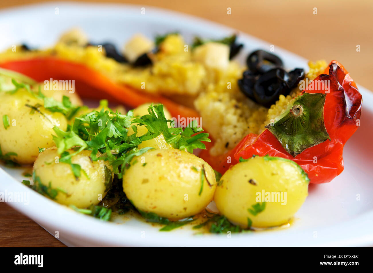 Il couscous riempite i peperoni con olive e formaggio vegan, servito con patate. Foto Stock