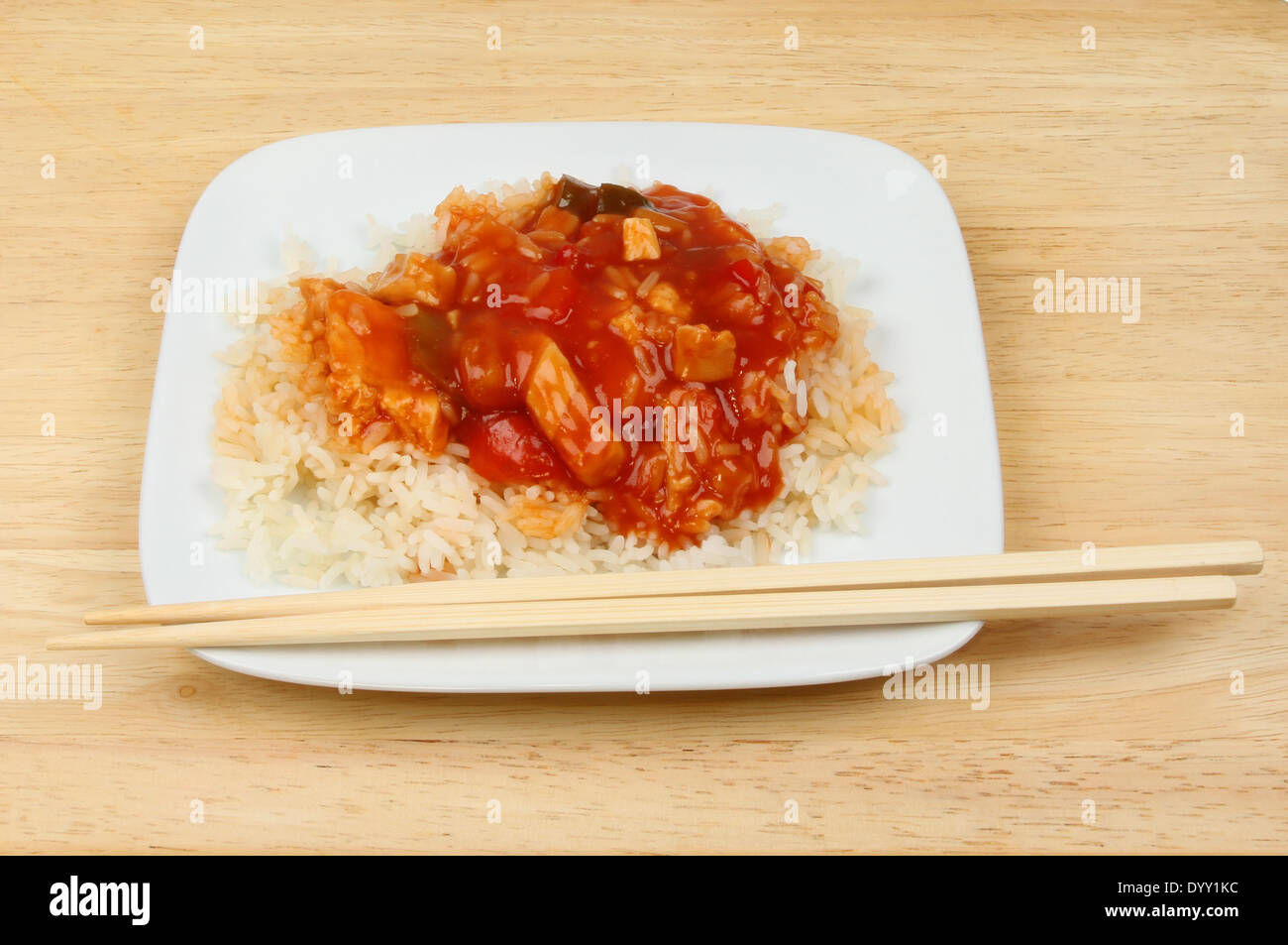 Pasto cinese, dolce e aspro di pollo con riso su una piastra con bacchette su una superficie in legno Foto Stock