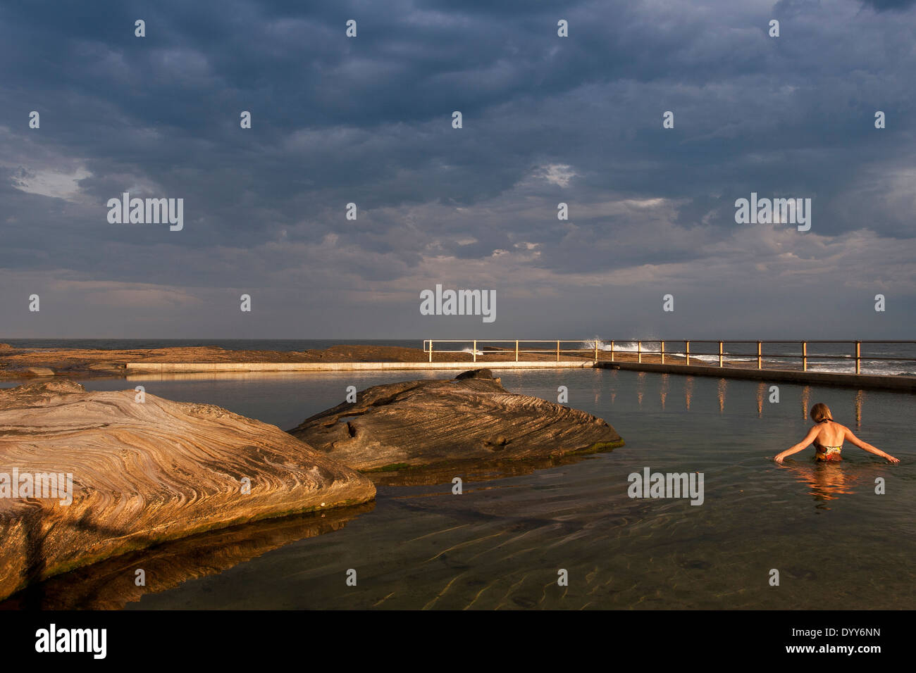 Ocean piscina costruita nel mare naturale-rocce. foto su molto ancora giorno con singolo nuotatore. nuvole temporalesche golden luce solare Australia Foto Stock