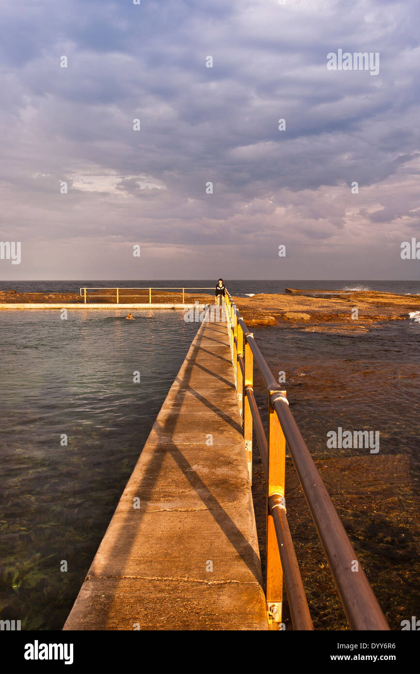 Vista oceano corrimano piscina costruita nel mare naturale-rocce. Ancora giorno. singolo nuotatore & persona a piedi bordo piscina Australia Foto Stock