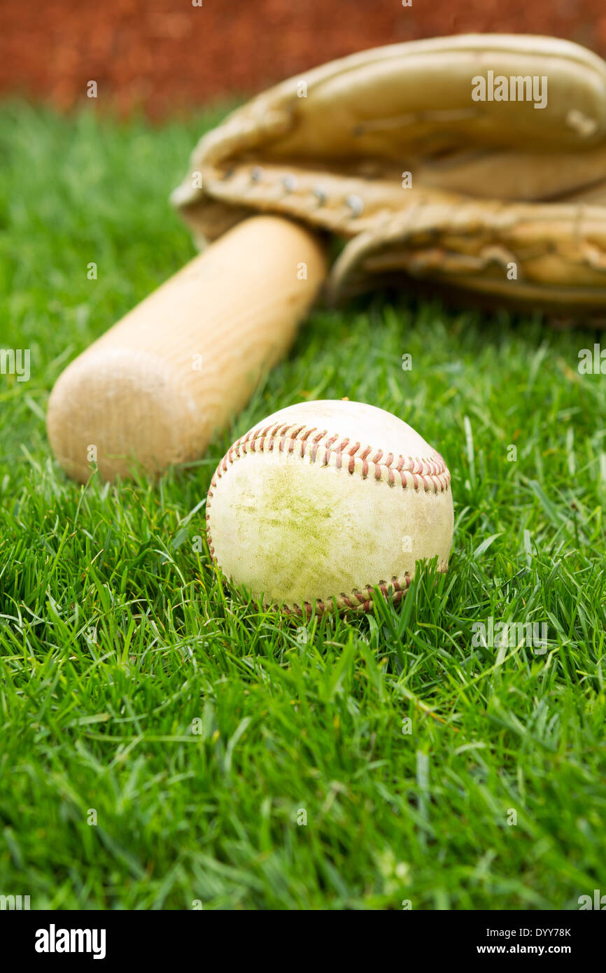 Foto verticale del vecchio, baseball bat e guanto con erba e red baseline in background Foto Stock
