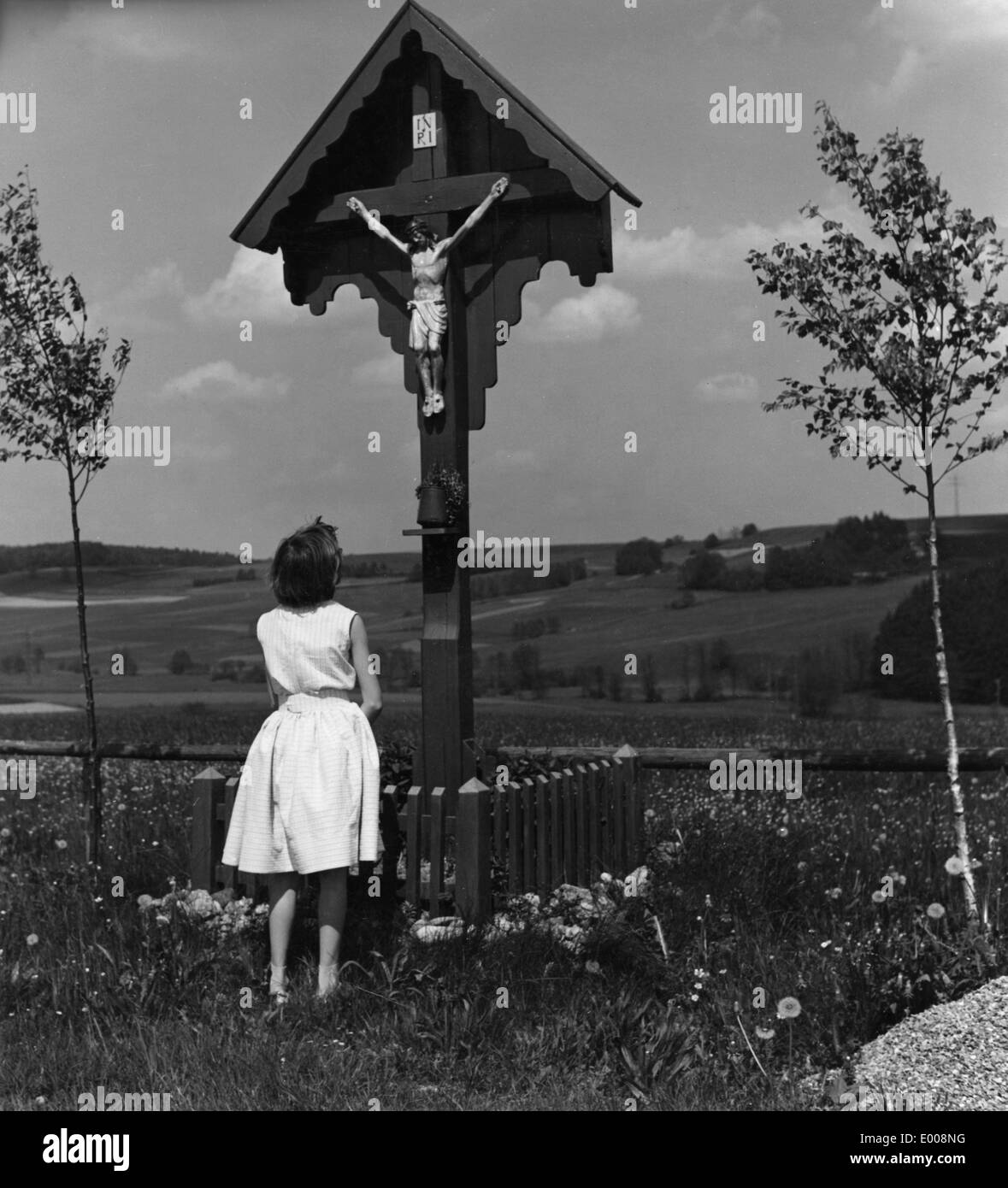 Una ragazza di fronte ad una croce lungo il tragitto, 50s Foto Stock