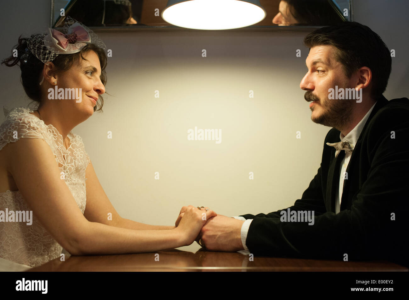 Felice sposa e lo sposo tenere le mani su un tavolo nella sala da pranzo sia a un matrimonio vintage Foto Stock