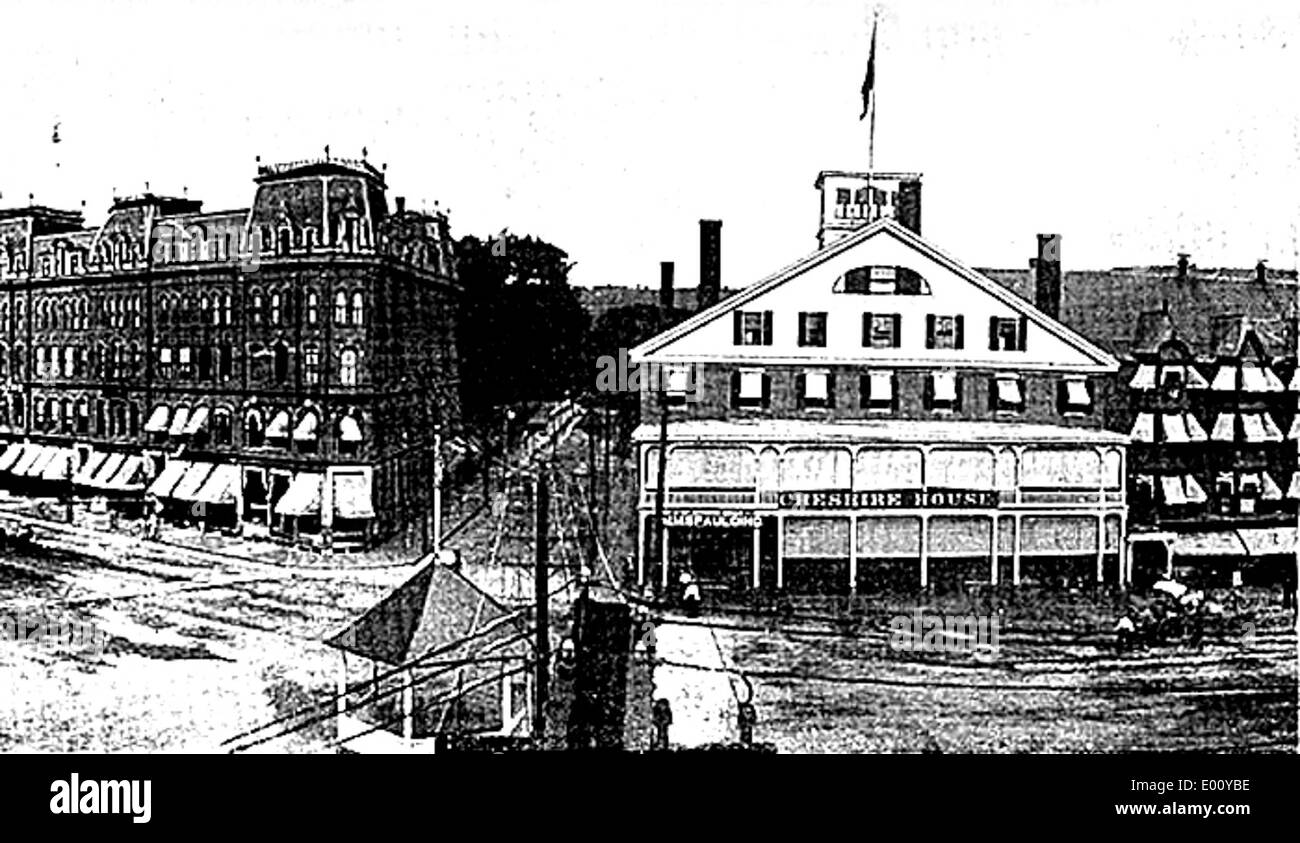 Questa fotografia storica cattura il lato est di Central Square a Keene, New Hampshire, mostrando l'architettura degli edifici locali, tra cui la Cheshire House. L'immagine riflette il vibrante quartiere finanziario di Keene, con vetrine e strade visibili che evidenziano il fascino e lo stile architettonico della città del XX secolo. Foto Stock