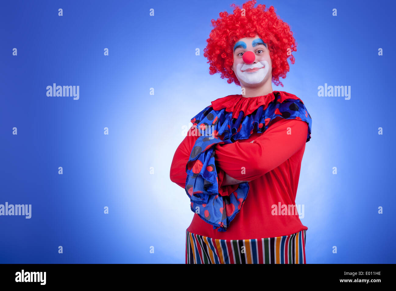 Sorridente clown di uomini in costume rosso su sfondo blu. Studio di illuminazione professionale Foto Stock