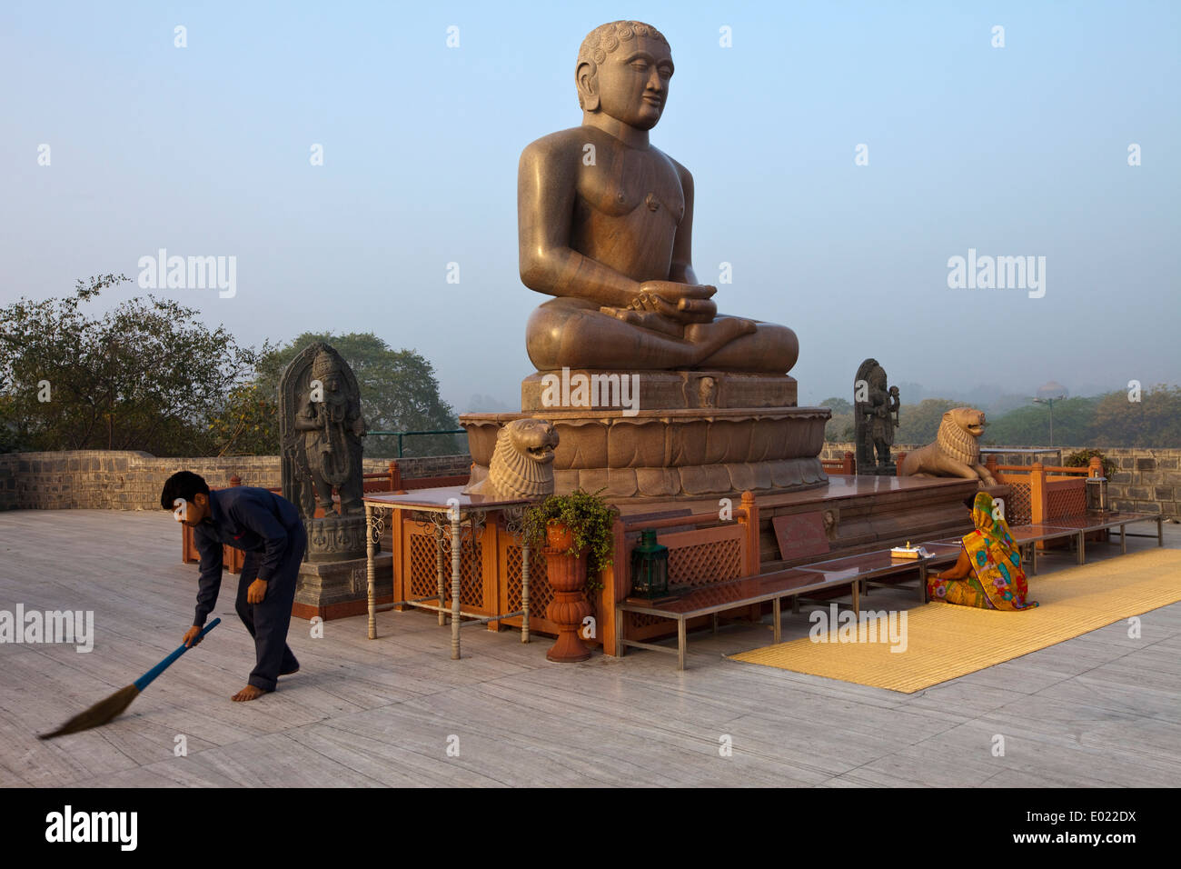 Un uomo spazza mentre una donna prega quasi all alba la statua di Lord Mahavira al Ahinsa Sthal tempio Jain, Delhi, India Foto Stock