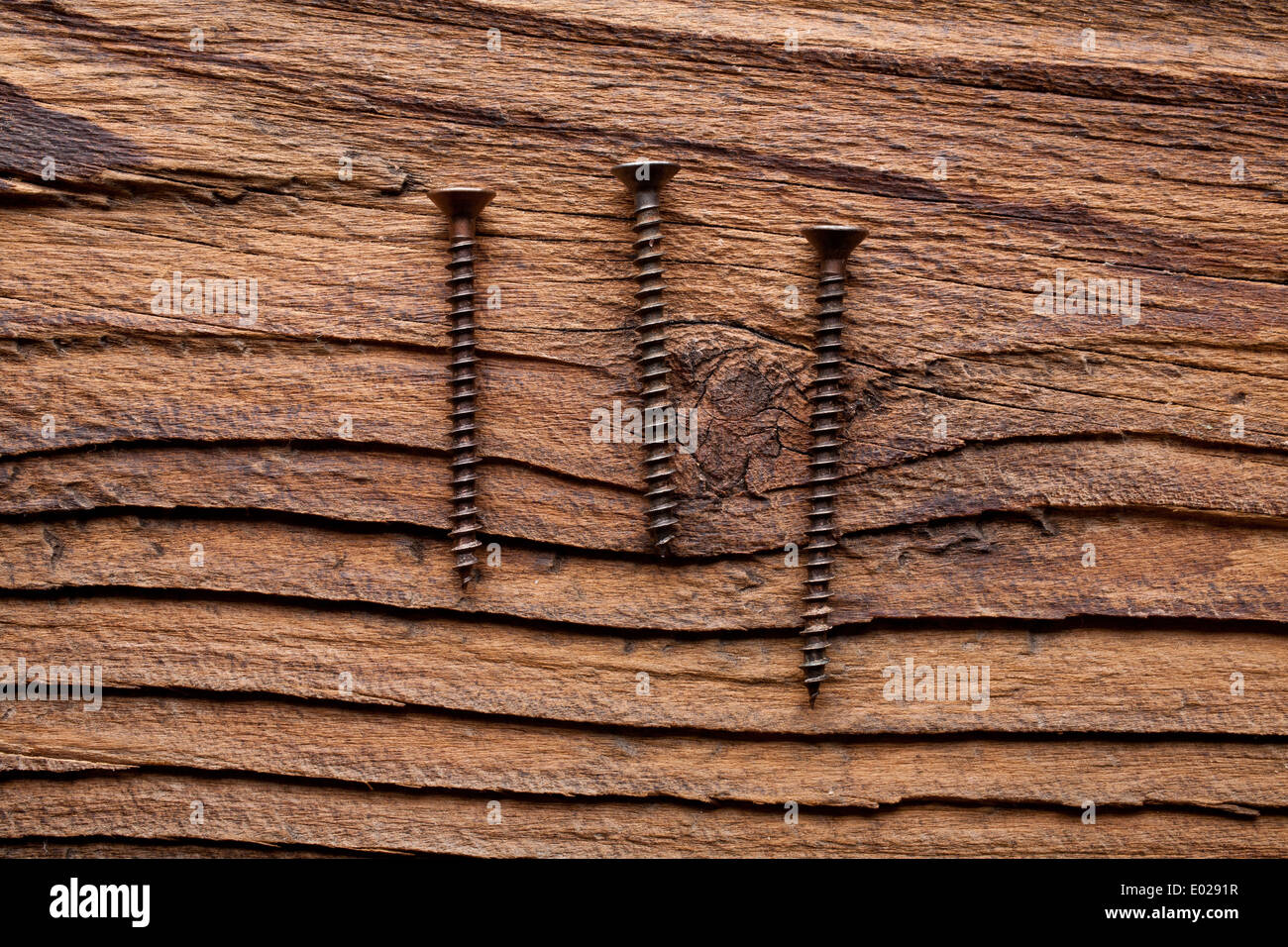 Un set di tre bronzato viti di rame su un buio a grana grossa sullo sfondo di legno Foto Stock