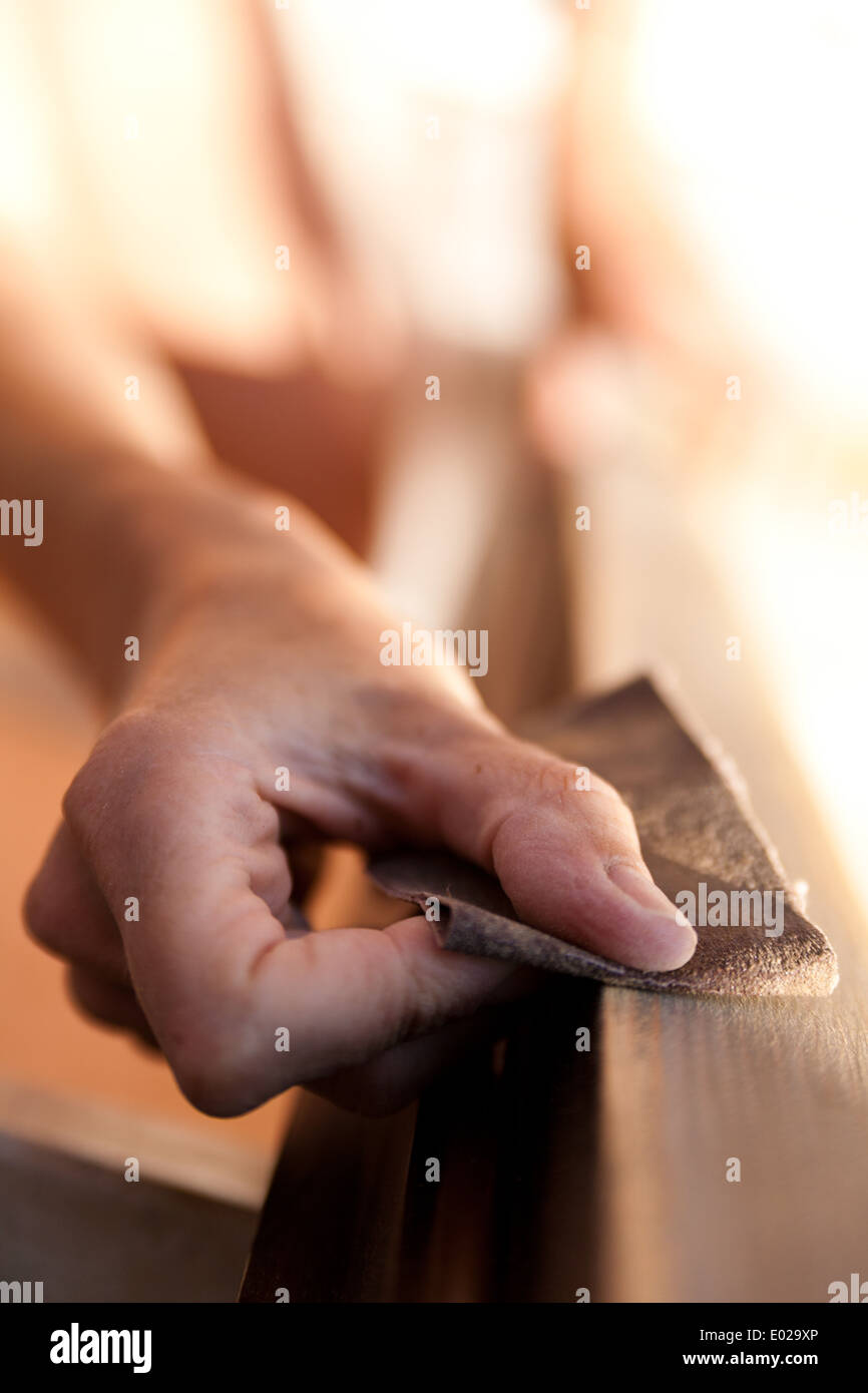 Le mani di una donna con la carta vetrata facendo lavori di DIY su infissi in legno Foto Stock