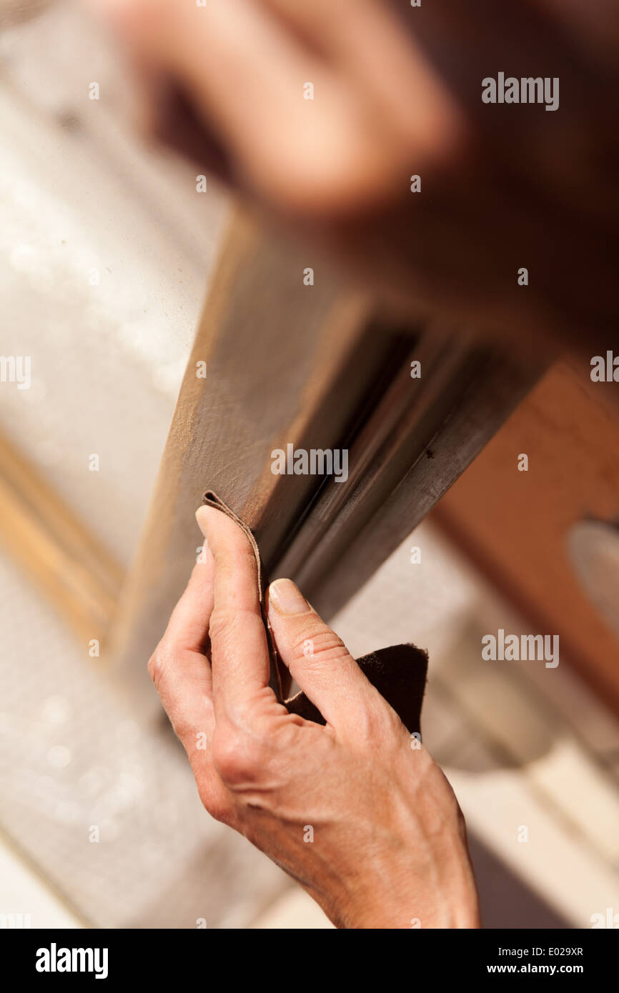 Le mani di una donna con la carta vetrata facendo lavori di DIY su infissi in legno Foto Stock