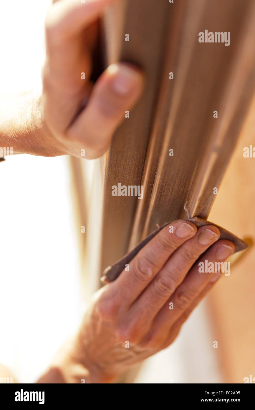 Le mani di una donna con la carta vetrata facendo lavori di DIY su infissi in legno Foto Stock