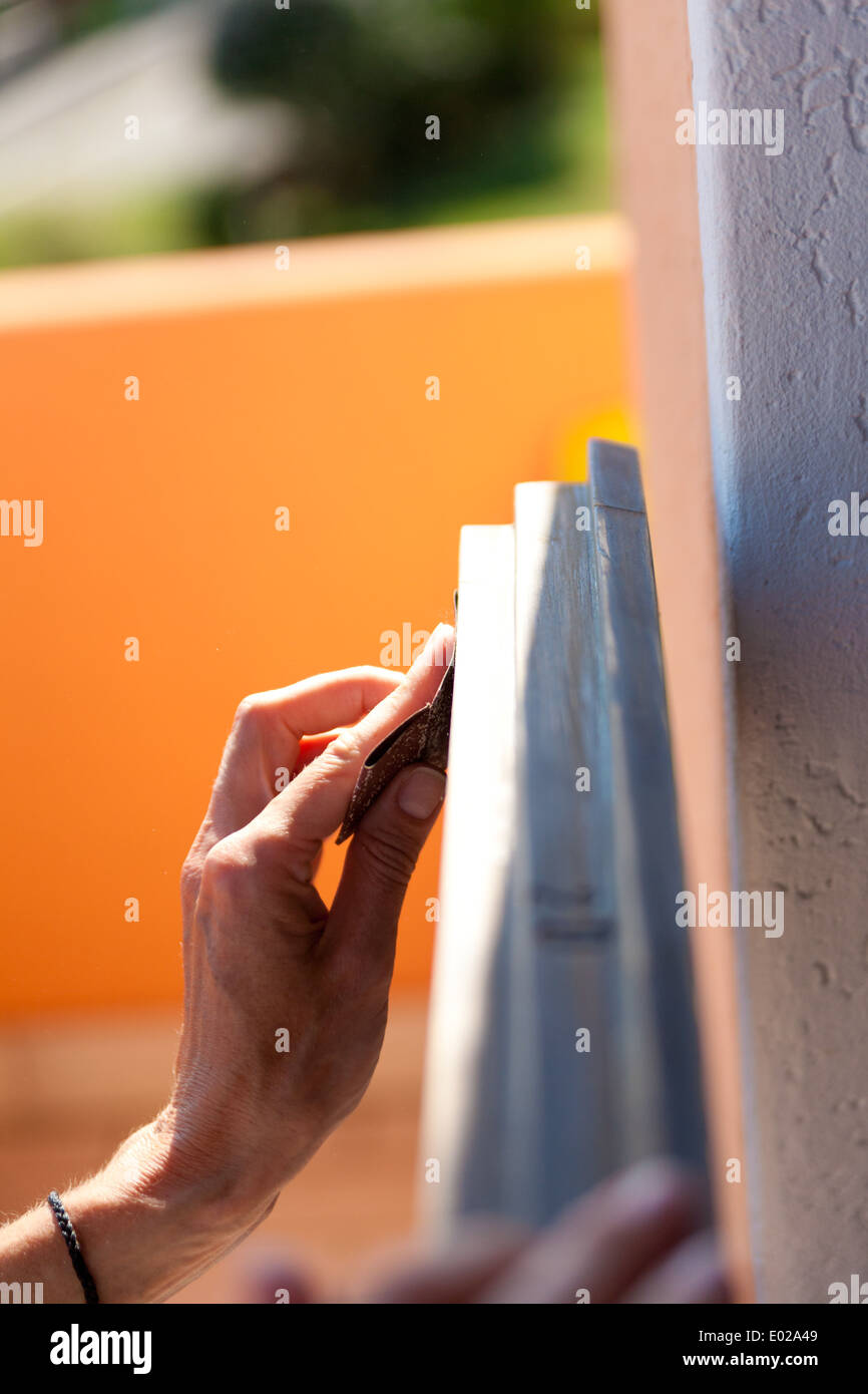 Le mani di una donna con la carta vetrata facendo lavori di DIY su infissi in legno Foto Stock