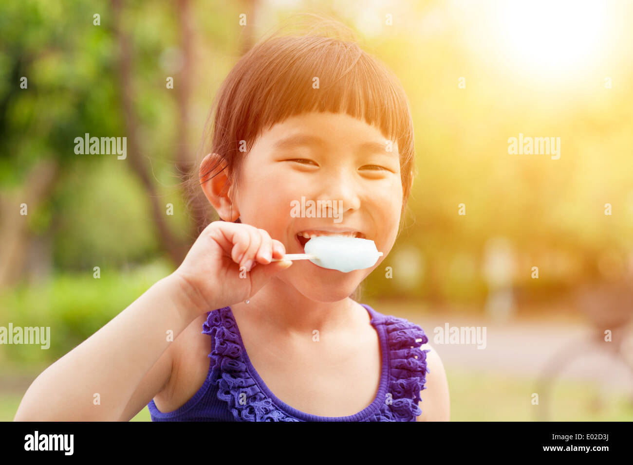 Felice bambina mangiare ghiaccioli con sfondo al tramonto Foto Stock