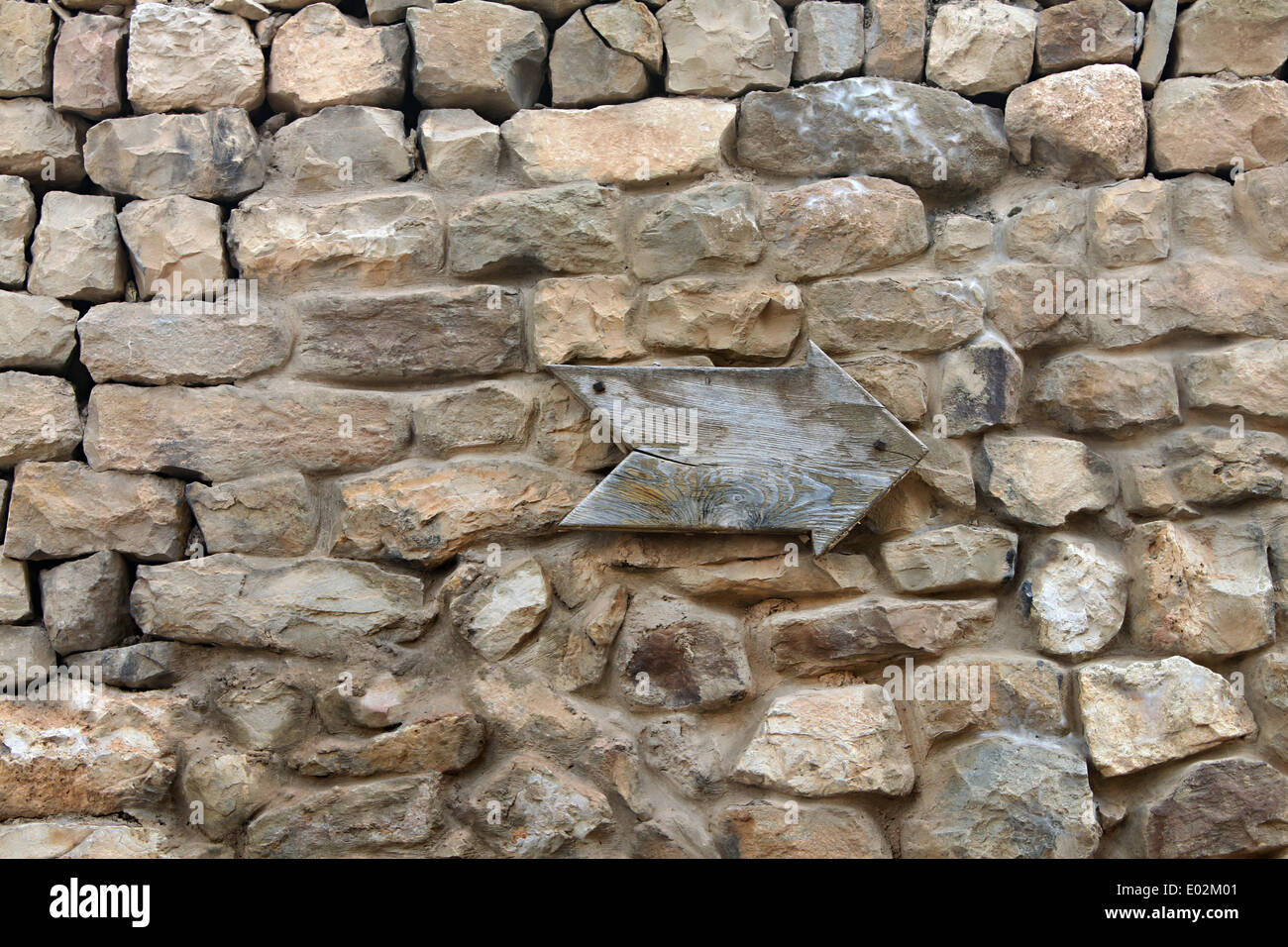 Una freccia in legno puntando su un vecchio muro di pietra. Foto Stock