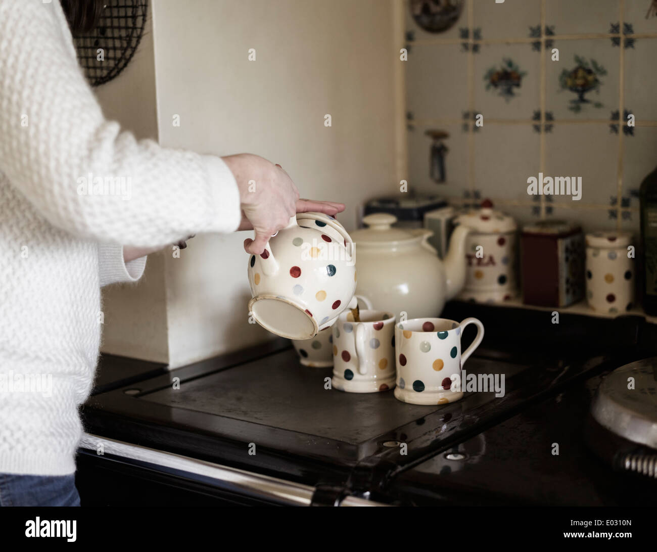 Una donna versando il tè da una gamma di cucina. Utilizzando la Cina decorativa. Foto Stock
