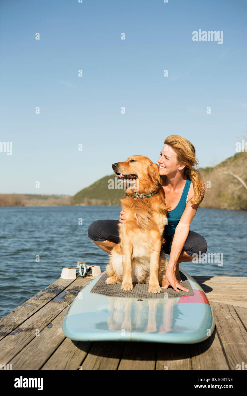 Una donna e un cane recuperatore su un paddleboard sul pontile. Foto Stock