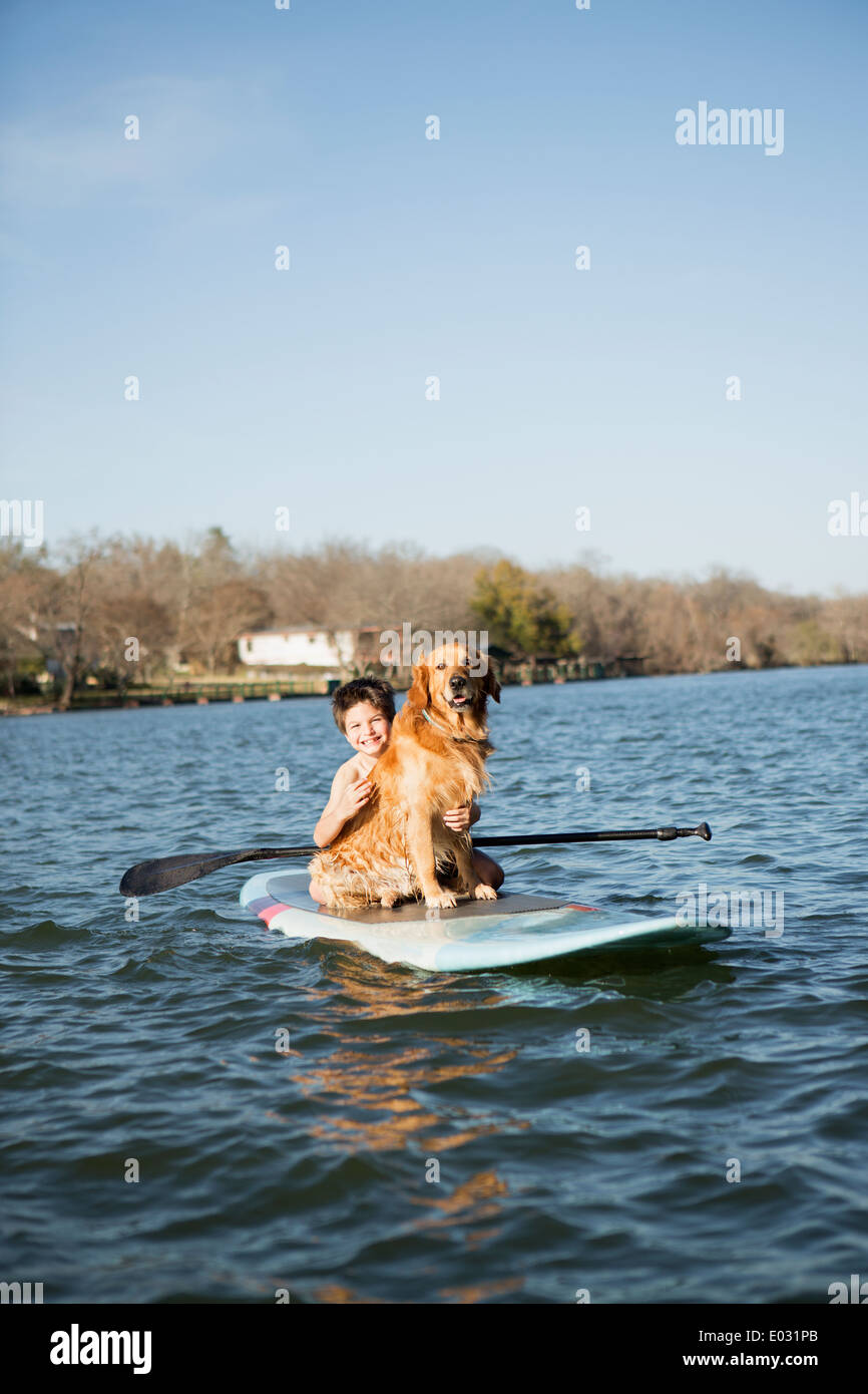Un bambino e un retriever dog sitter su un paddleboard sull'acqua. Foto Stock