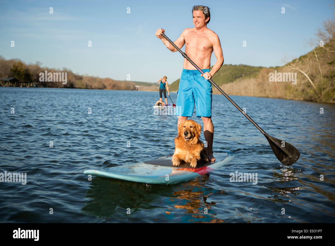 Un uomo in piedi su un paddleboard con un cane. Foto Stock