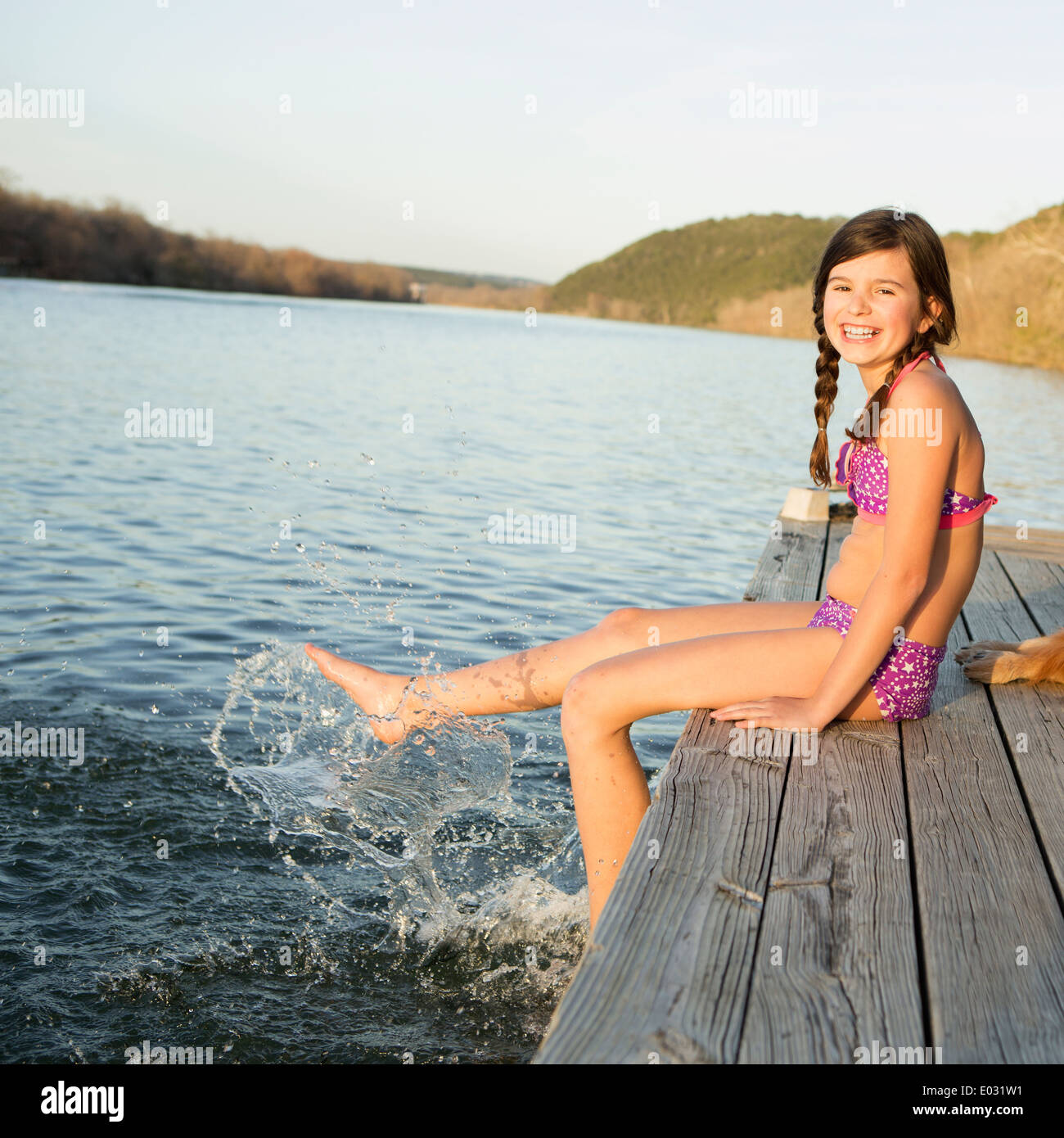 Una ragazza in un bikini seduto su di un molo con i suoi piedi nell'acqua. Foto Stock