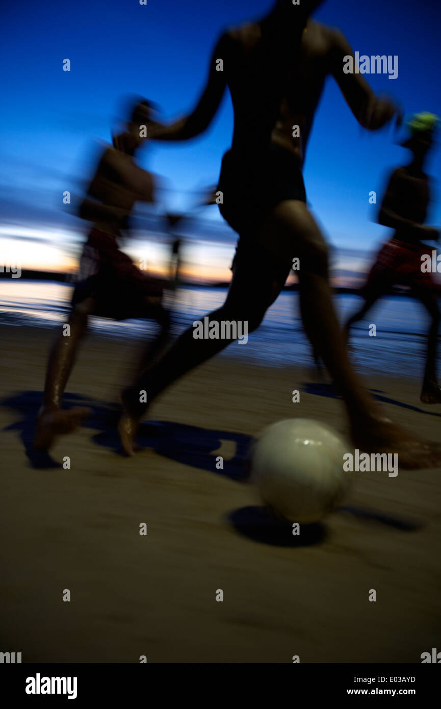 Il calcio brasiliano i giocatori a caccia di pallone da calcio di notte sulla spiaggia in una sfocatura in Nordeste Bahia Brasile Foto Stock
