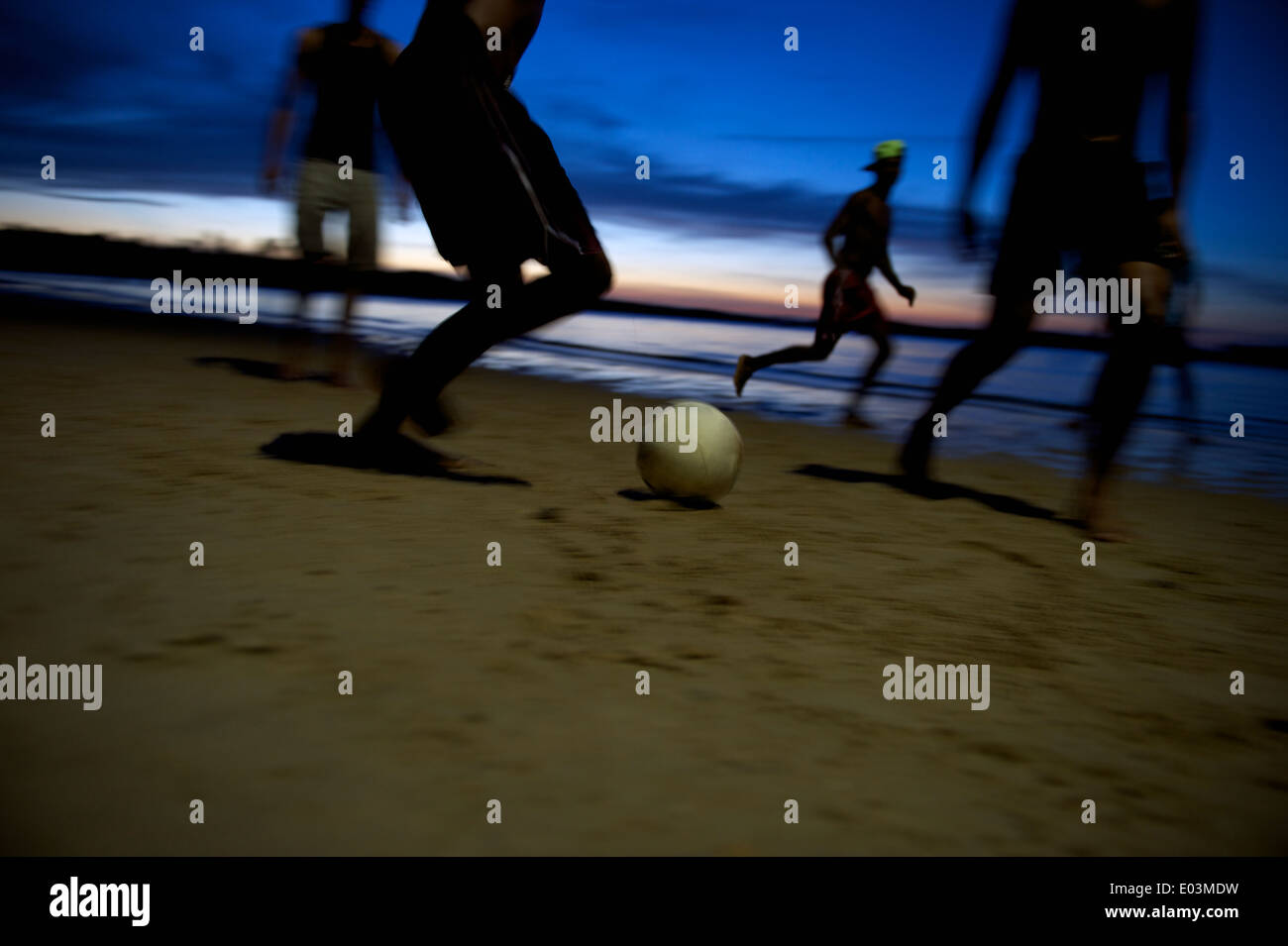 Il calcio brasiliano i giocatori di calcio in esecuzione durante la notte sulla spiaggia in una sfocatura di sagome ombra sulla riva del fiume del Brasile Foto Stock
