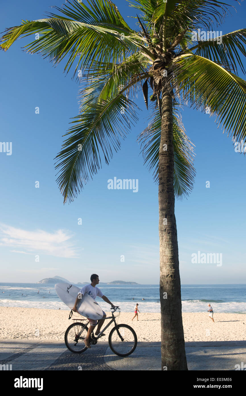 RIO DE JANEIRO, Brasile - 21 febbraio 2014: uomo cavalca una bicicletta che trasportano le tavole da surf lungo la passerella a Arpoador lungo una vista Foto Stock