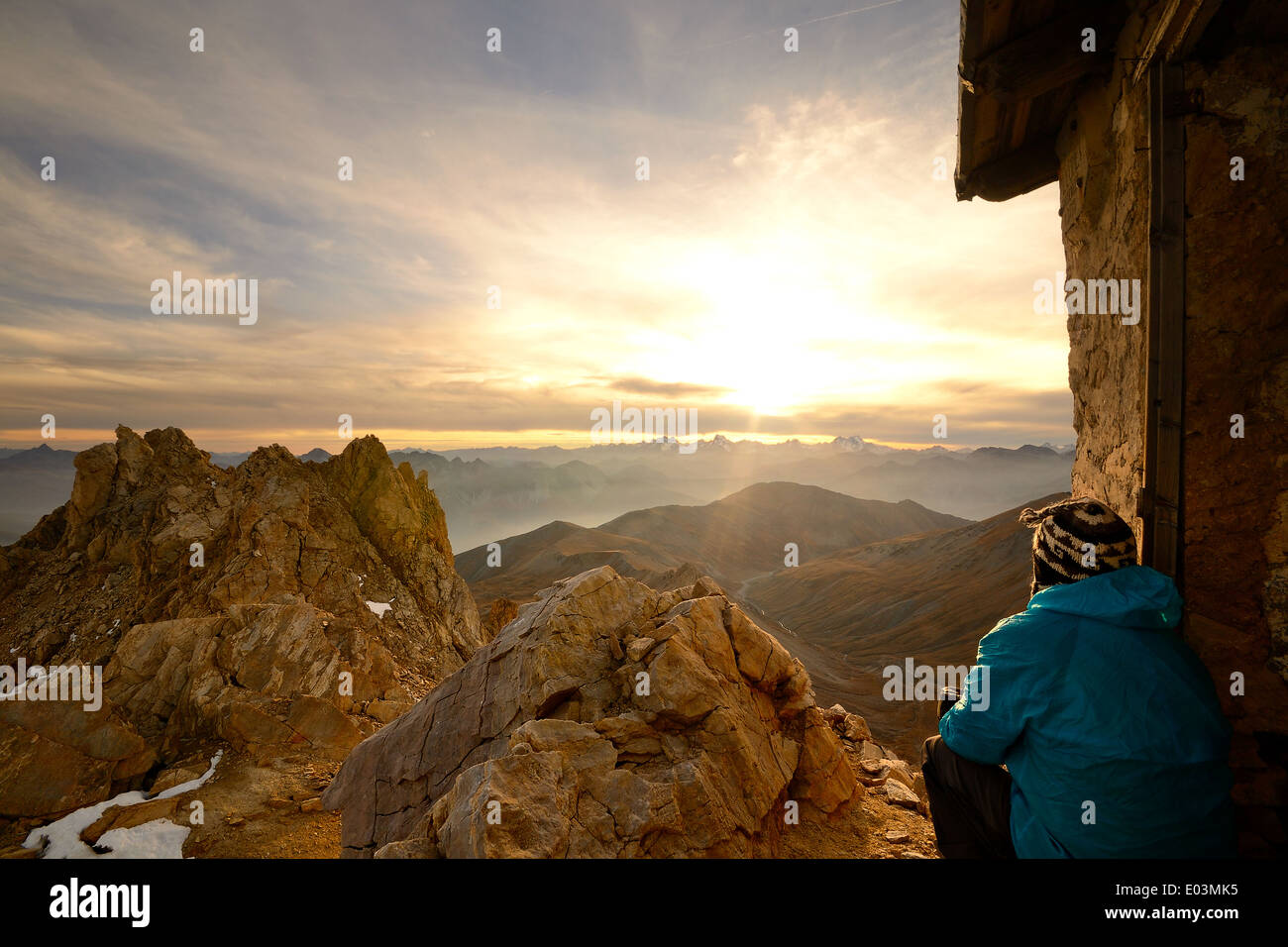 Escursionista seduto vicino a capanna e guardando un tramonto mozzafiato dalla cima delle montagne rocciose in italiano - Le Alpi francesi. Foto Stock