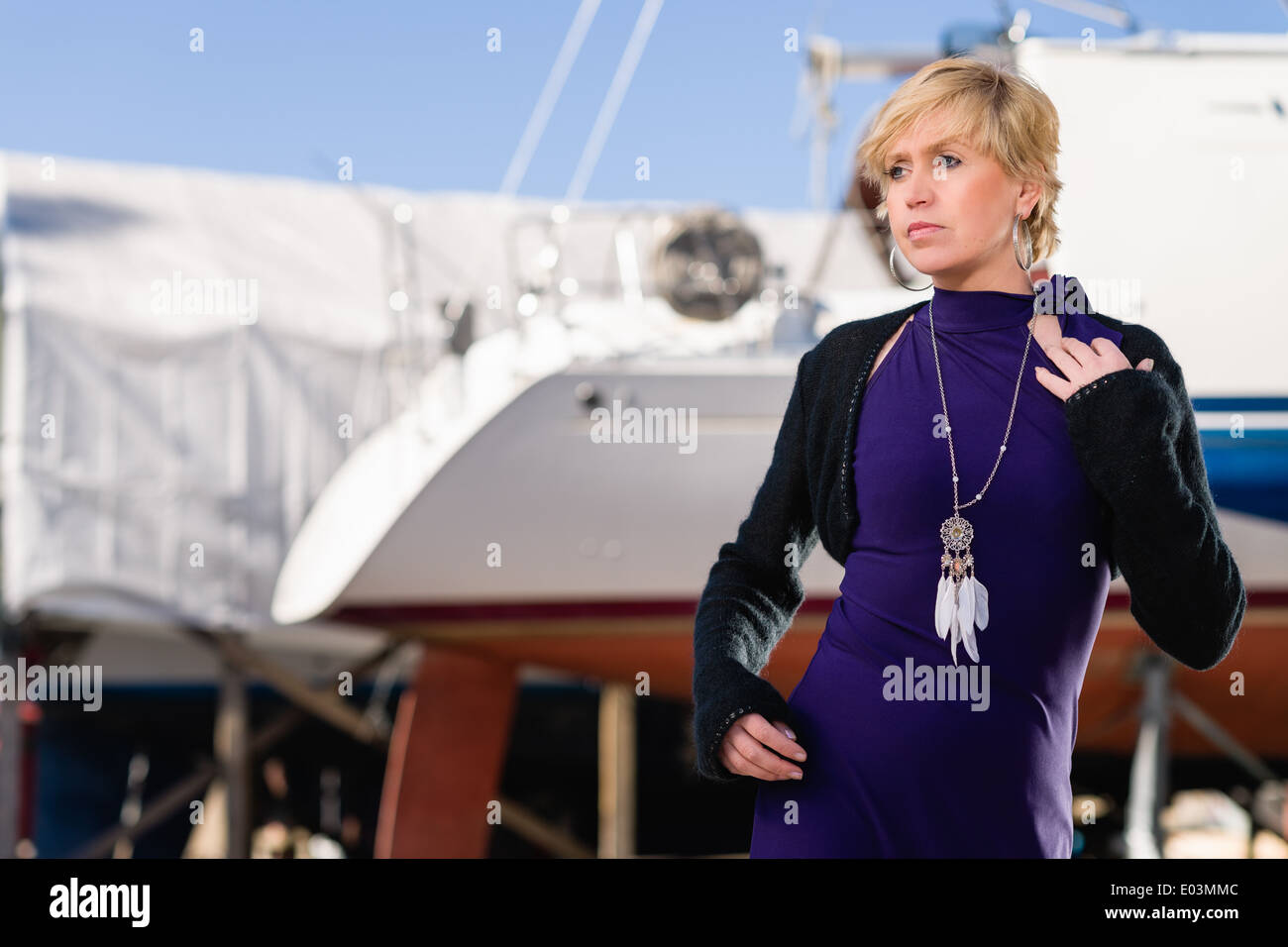 Donna matura indossando abito viola e posa, barca a vela sullo sfondo Foto Stock