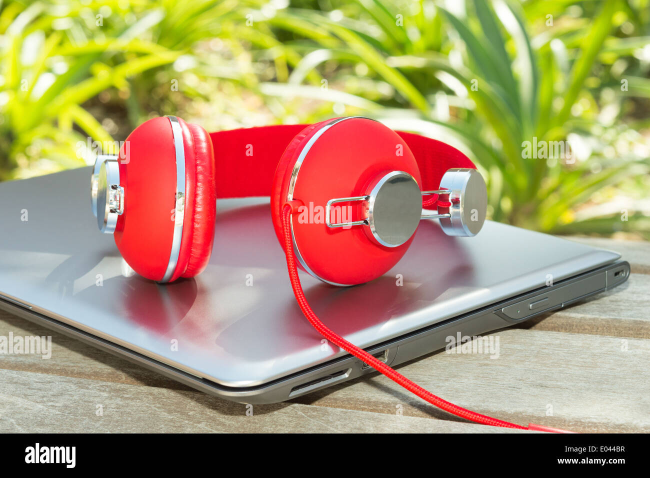 Rosso vivo le cuffie e il laptop sulla panca di legno in posizione di parcheggio Foto Stock