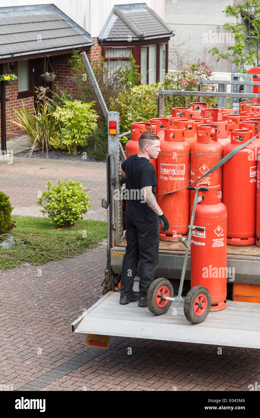 Un uomo di consegna Consegna famiglia red Calor Gas bottiglie su un pickup carrello elevatore di coda al di fuori di una struttura interna. Regno Unito, Gran Bretagna. Foto Stock