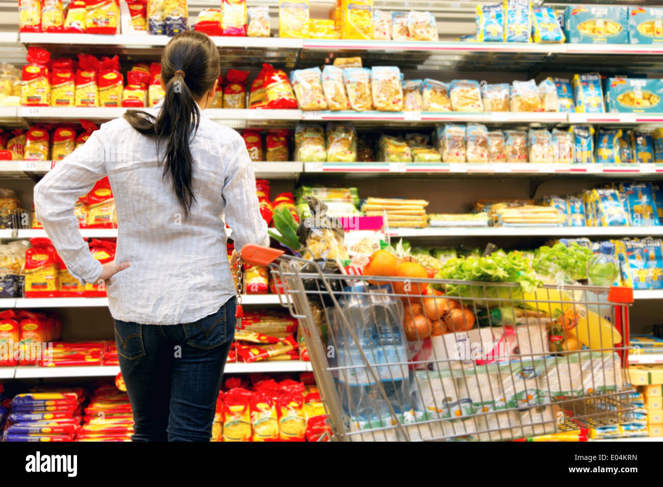 Giovane donna di stato prima di archiviare in un supermercato, Junge Frau steht vor Regal in einem Supermarkt Foto Stock