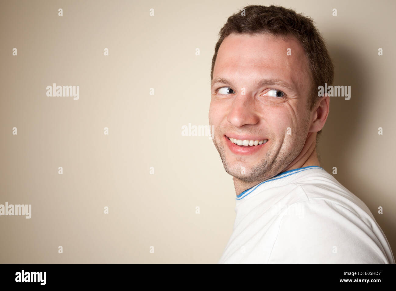 Sorridente giovane uomo caucasico in t-shirt bianco sopra la parete grigia Foto Stock