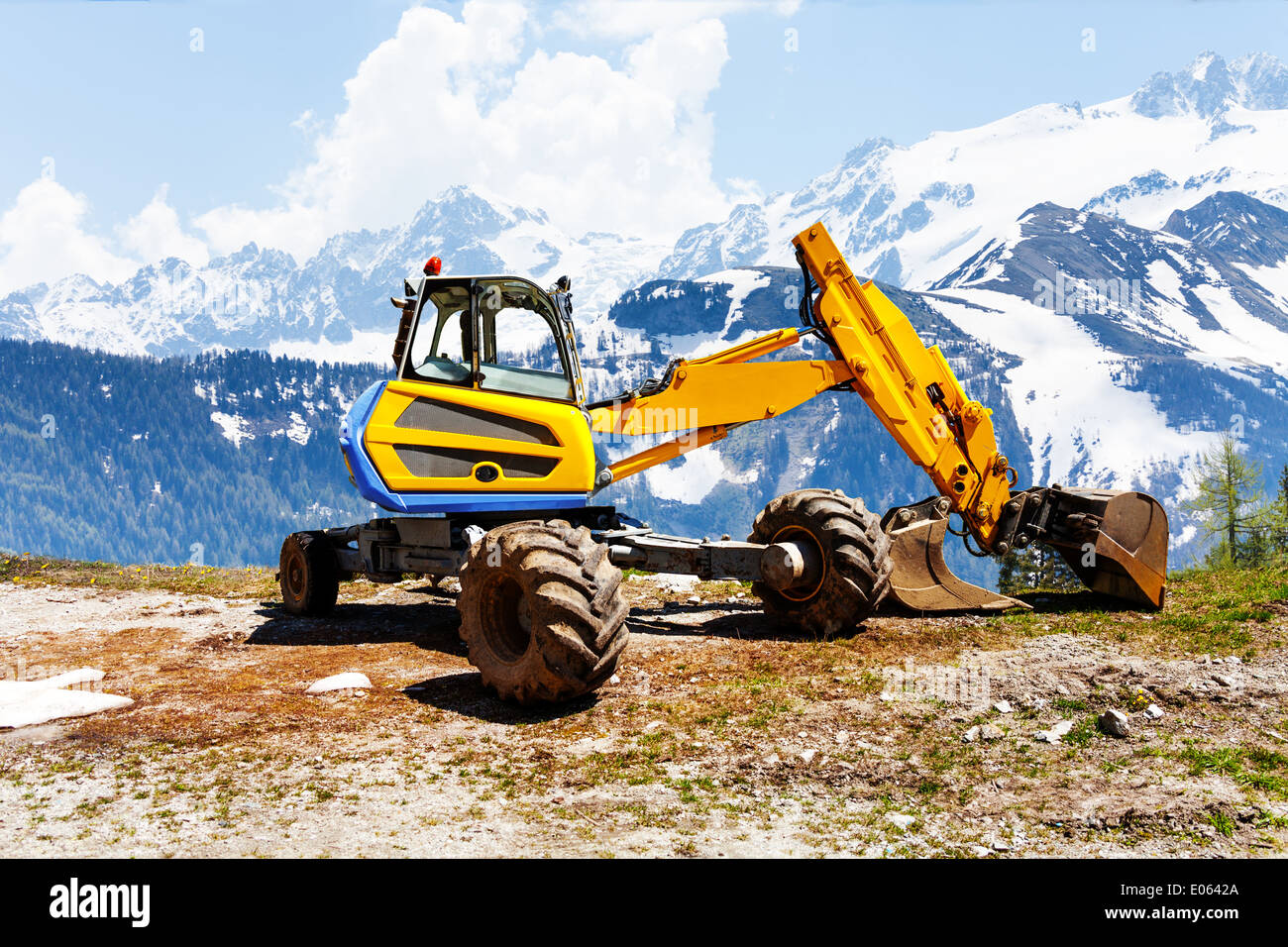 Escavatore giallo lavorare vicino alle montagne Foto Stock