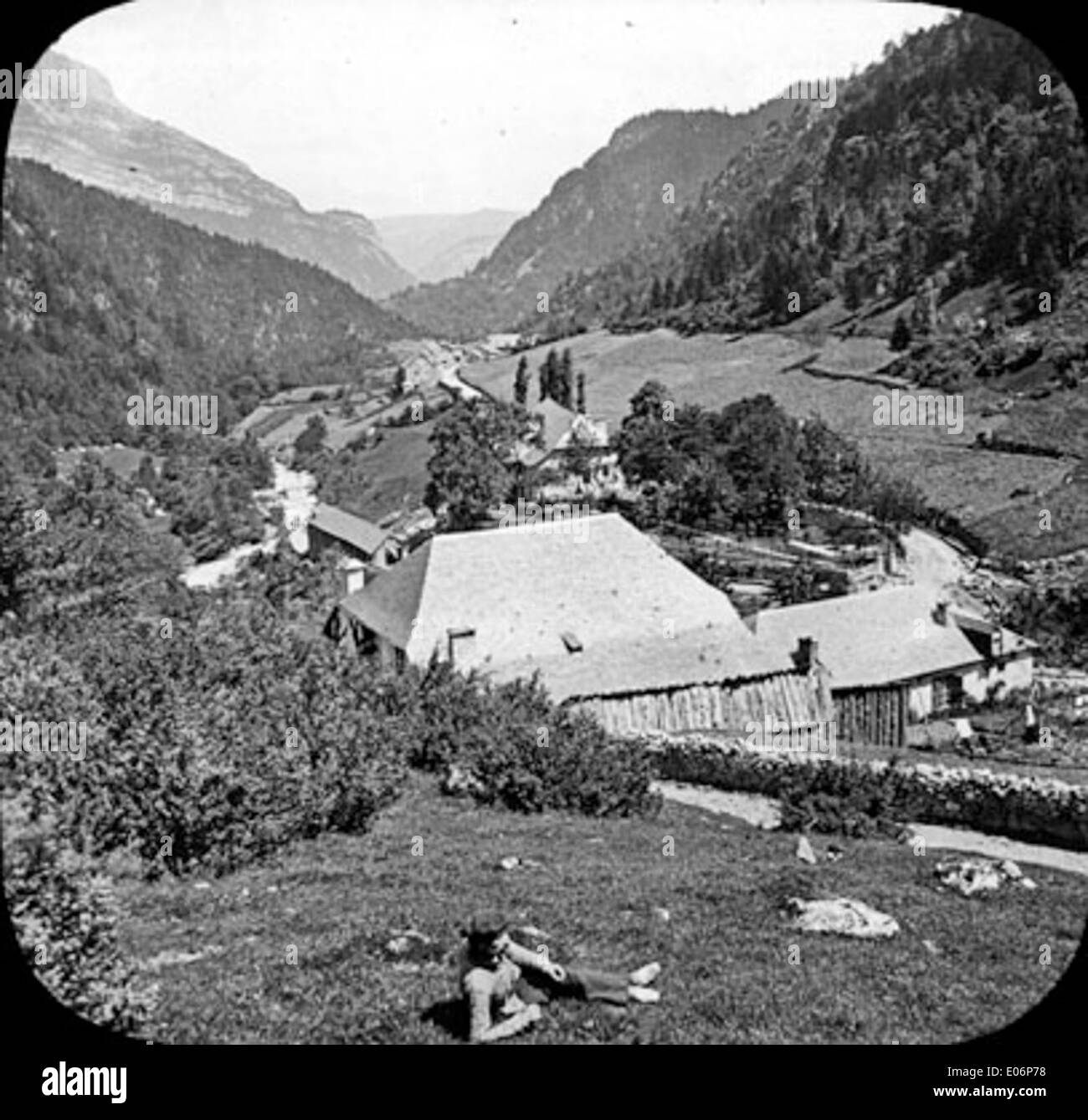 Una foto in bianco e nero di Gabas nella Vallée d'Ossau, che mostra una città collinare con tetti in primo piano e una donna seduta nell'erba. Foto Stock Una foto in bianco e nero di Gabas nella Vallée d'Ossau, che mostra una città collinare con tetti in primo piano e una donna seduta nell'erba. Foto Stock