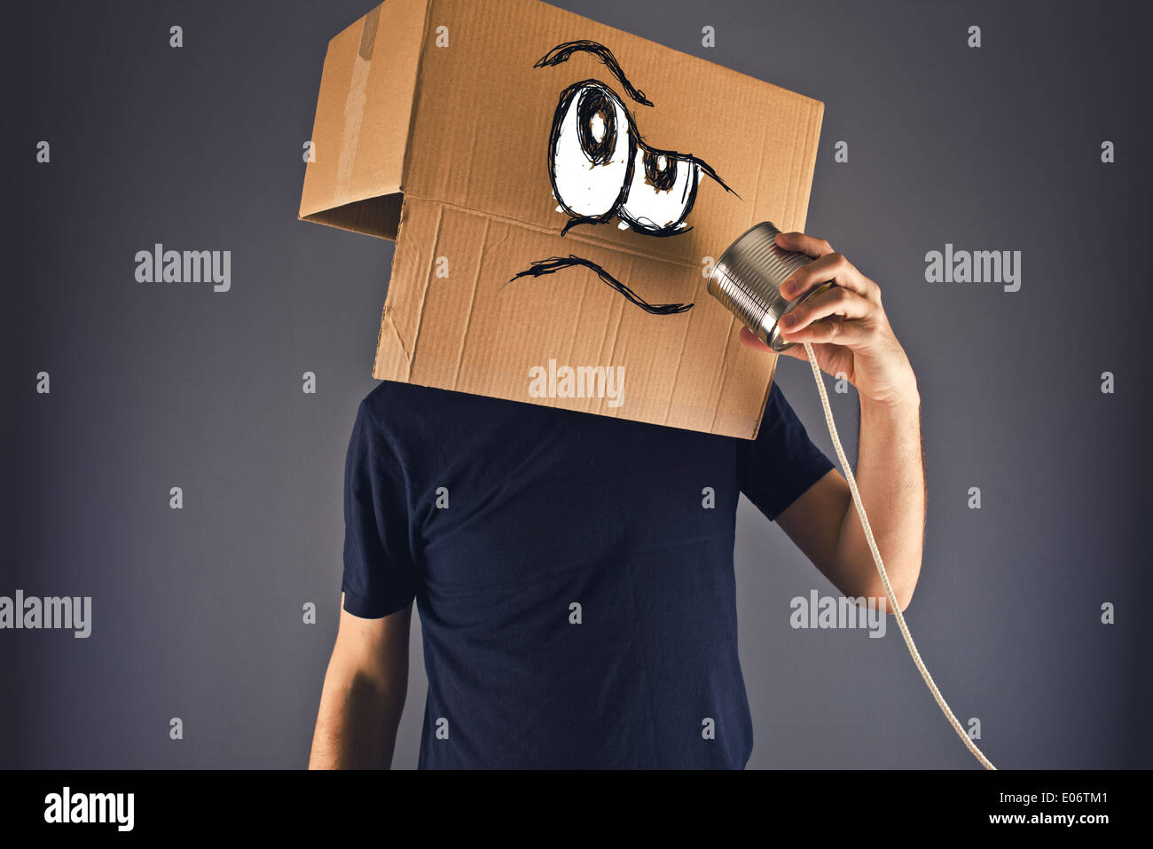 Uomo con scatola di cartone sulla sua testa usando stagno possono telefonare per la conversazione. Viso arrabbiato espressione. Foto Stock