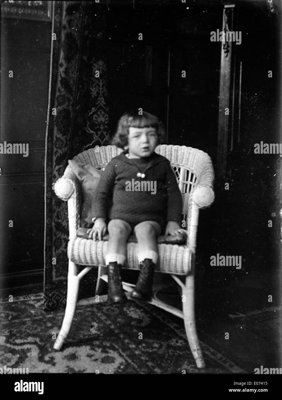 Petit garçon assis dans un fauteuil en rotin Foto Stock