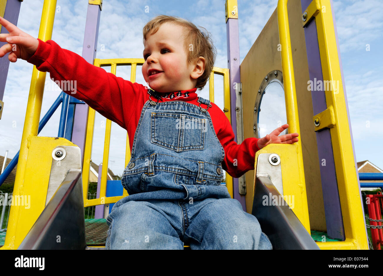Un bimbo di 2 anni giocando su una diapositiva in un parco giochi Foto Stock