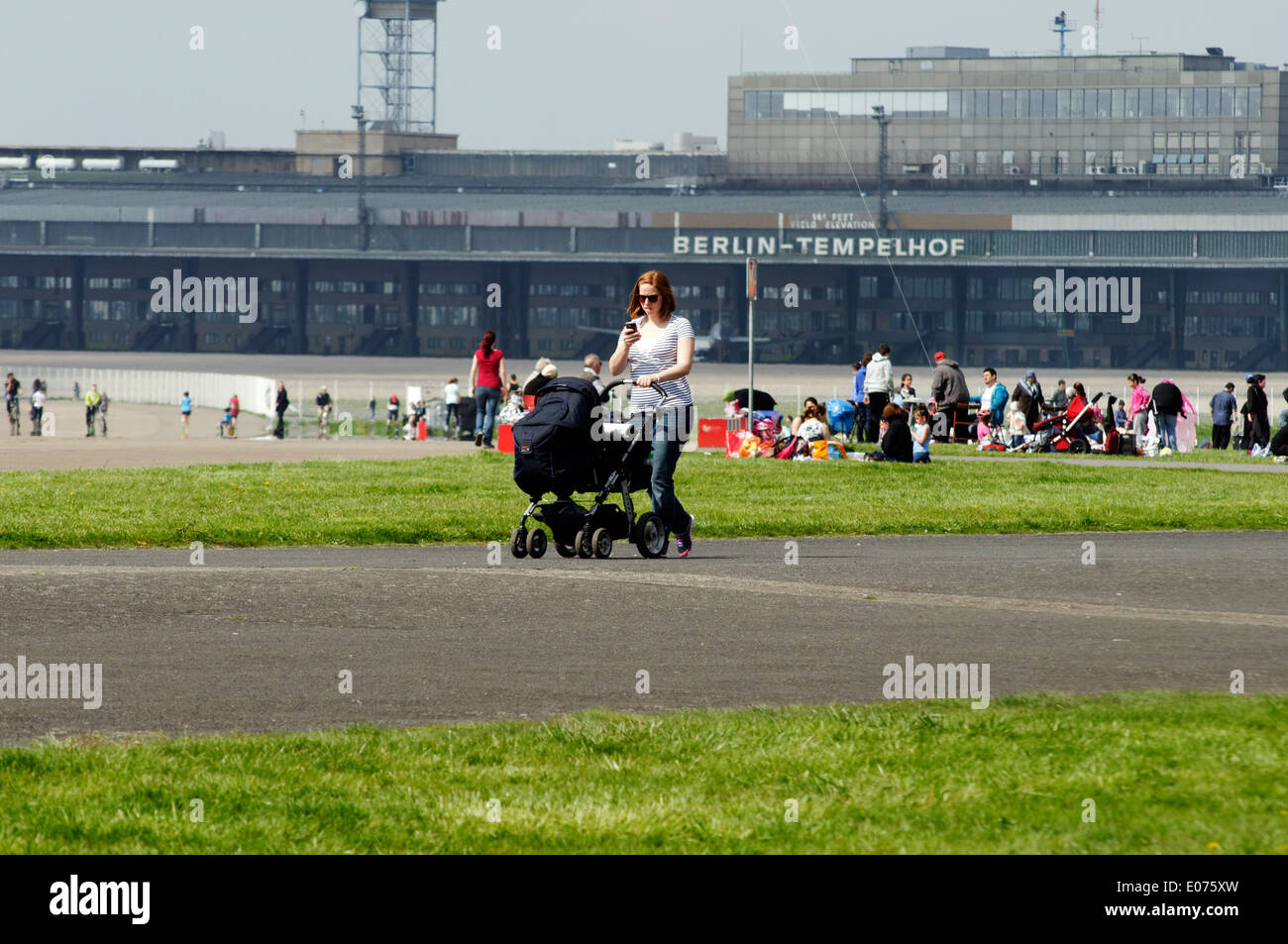 Una donna che spinge la PRAM e guardando il suo telefono mobile a Berlino Tempelhof di Berlino, ora un ampio parco Foto Stock