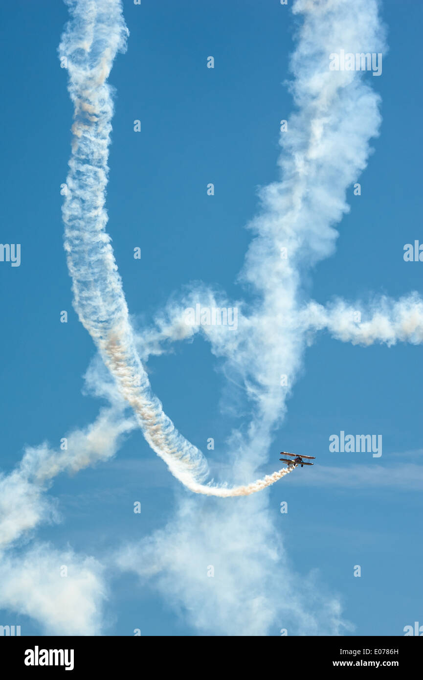 Flumes bianco di fumo contrassegnare il percorso ciclico di un biplano mentre wingwalker Jane vimini trattiene saldamente ad un'ala. Foto Stock