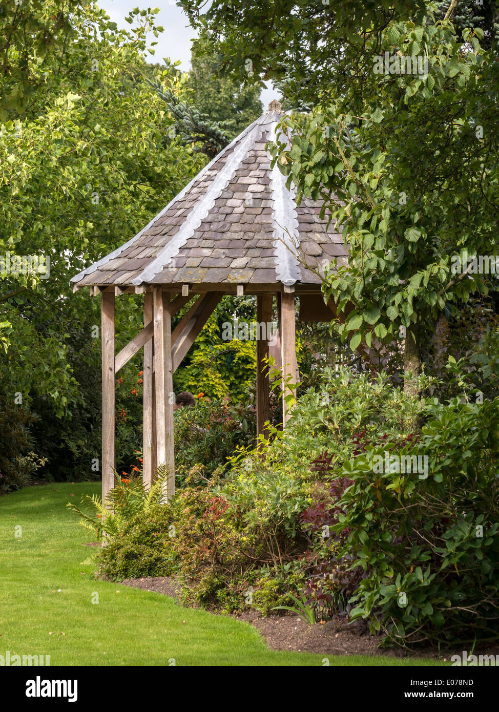 Gazebo ottagonale con spioventi del tetto di ardesia e rovere montante e traversa telaio in giardino con prato alberi e arbusti Foto Stock
