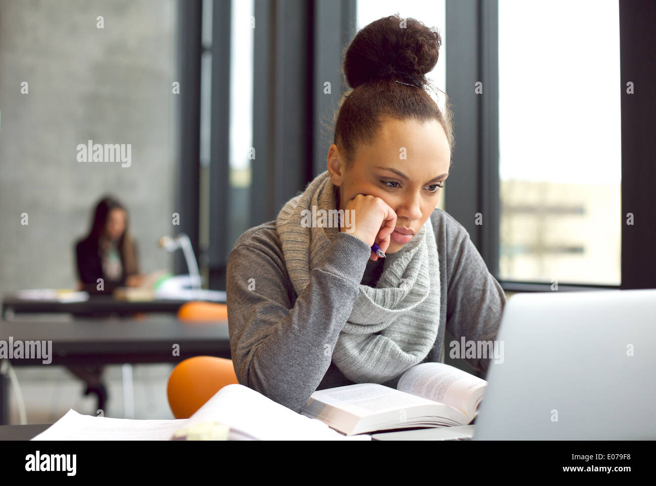 Grave giovane studentessa si concentra sul suo computer portatile mentre studiano in una libreria. Giovane donna seduta a tavola e la lettura. Foto Stock
