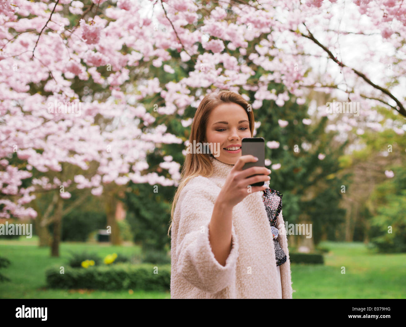 Bella giovane femmina di fotografare con lo smartphone a primavera sbocciano i fiori parco. Femmina caucasica tiro al parco con telefono. Foto Stock