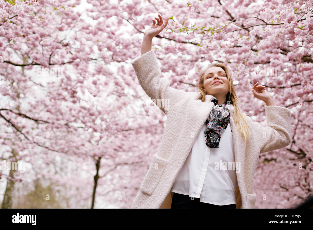 Giovane donna a braccia alzate godersi l'aria fresca nella primavera del parco. Spensierato giovane femmina a molla blossom garden - all'aperto Foto Stock