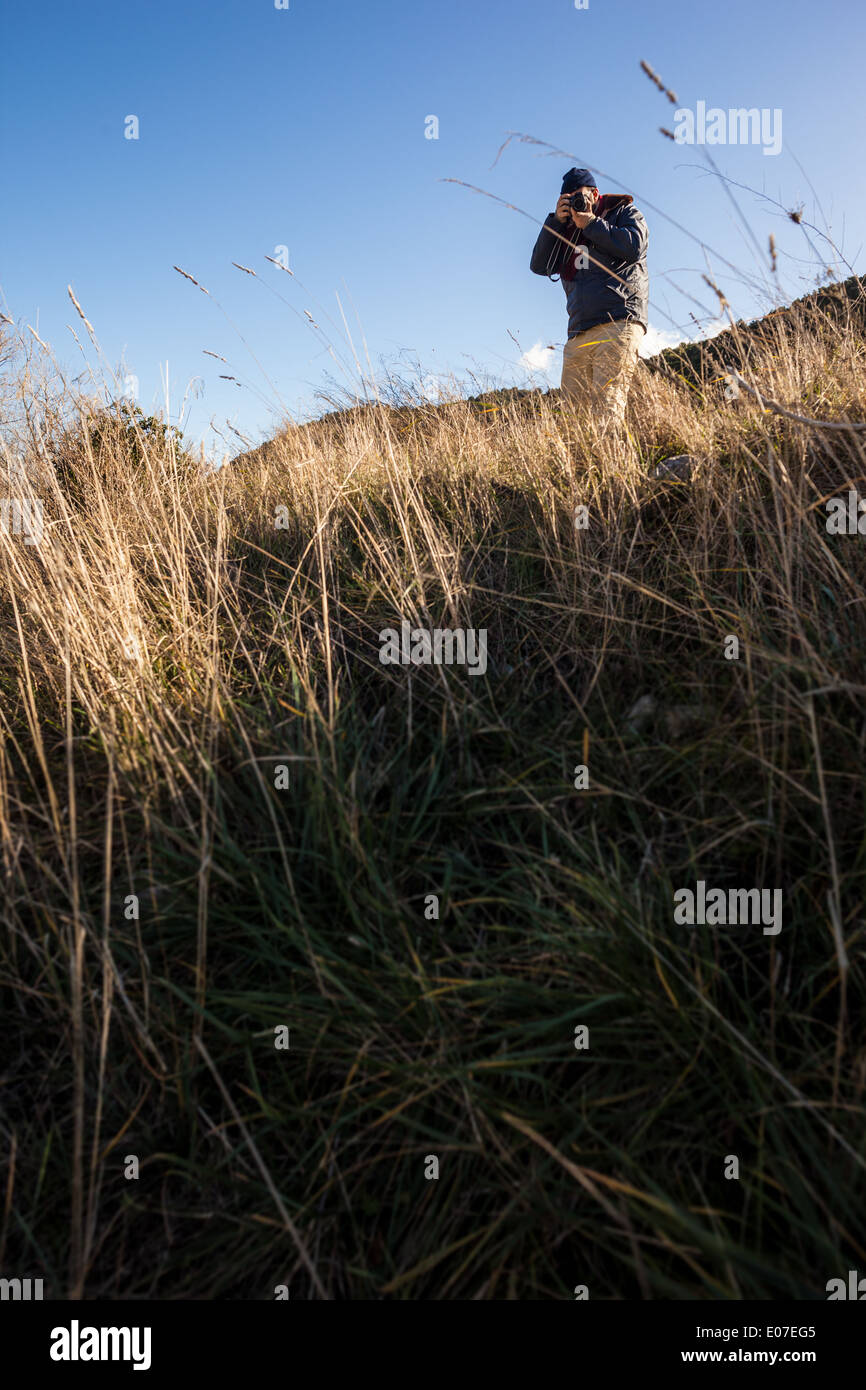 Un uomo di escursionismo e riprese con una fotocamera reflex digitale a obiettivo singolo Foto Stock
