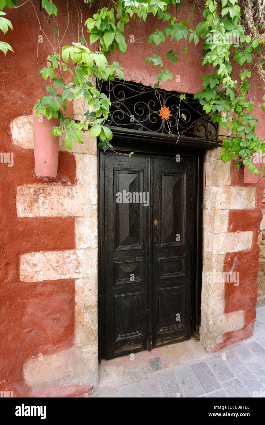 Rosso rustico in pietra color crema parete di casa con porta di legno scuro drappeggiati con vegetazione Chania old town Creta Grecia situato sul Foto Stock