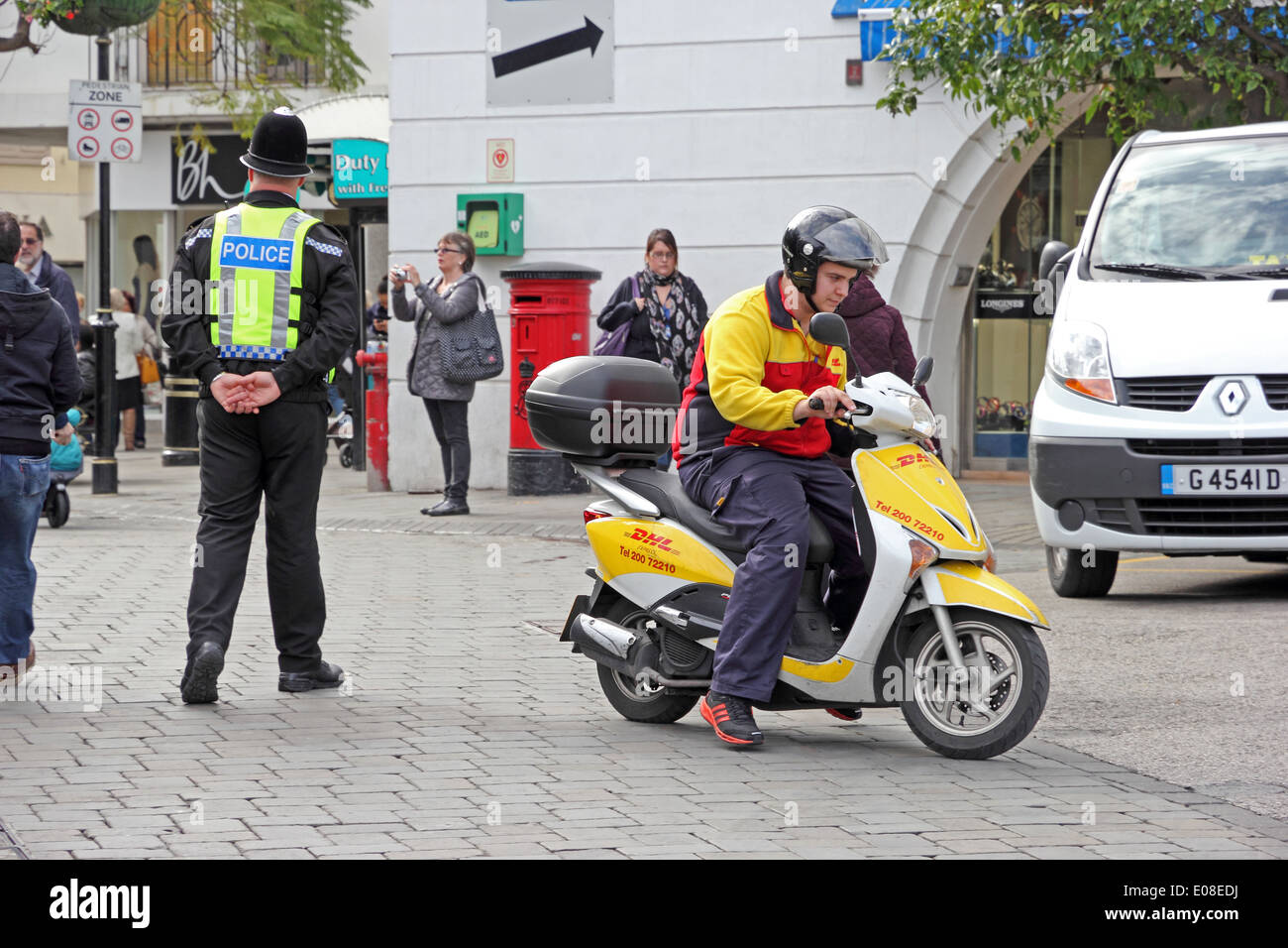 Corriere DHL su scooter con un poliziotto in background Foto Stock