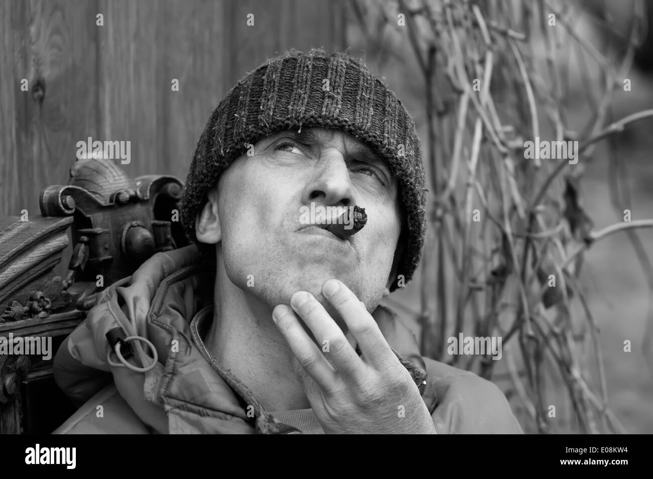 Uomo che indossa un cappello e giacca con cappuccio di fumare con un sguardo distante. Concetto di sognatore, outdoor shot. In bianco e nero. Foto Stock